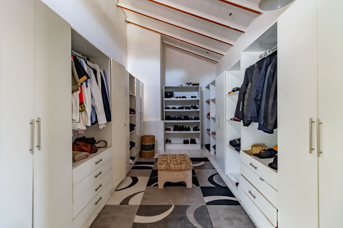 A spacious walk-in closet featuring extensive built-in cabinetry, shelving, and drawers with a vaulted ceiling and exposed beams.