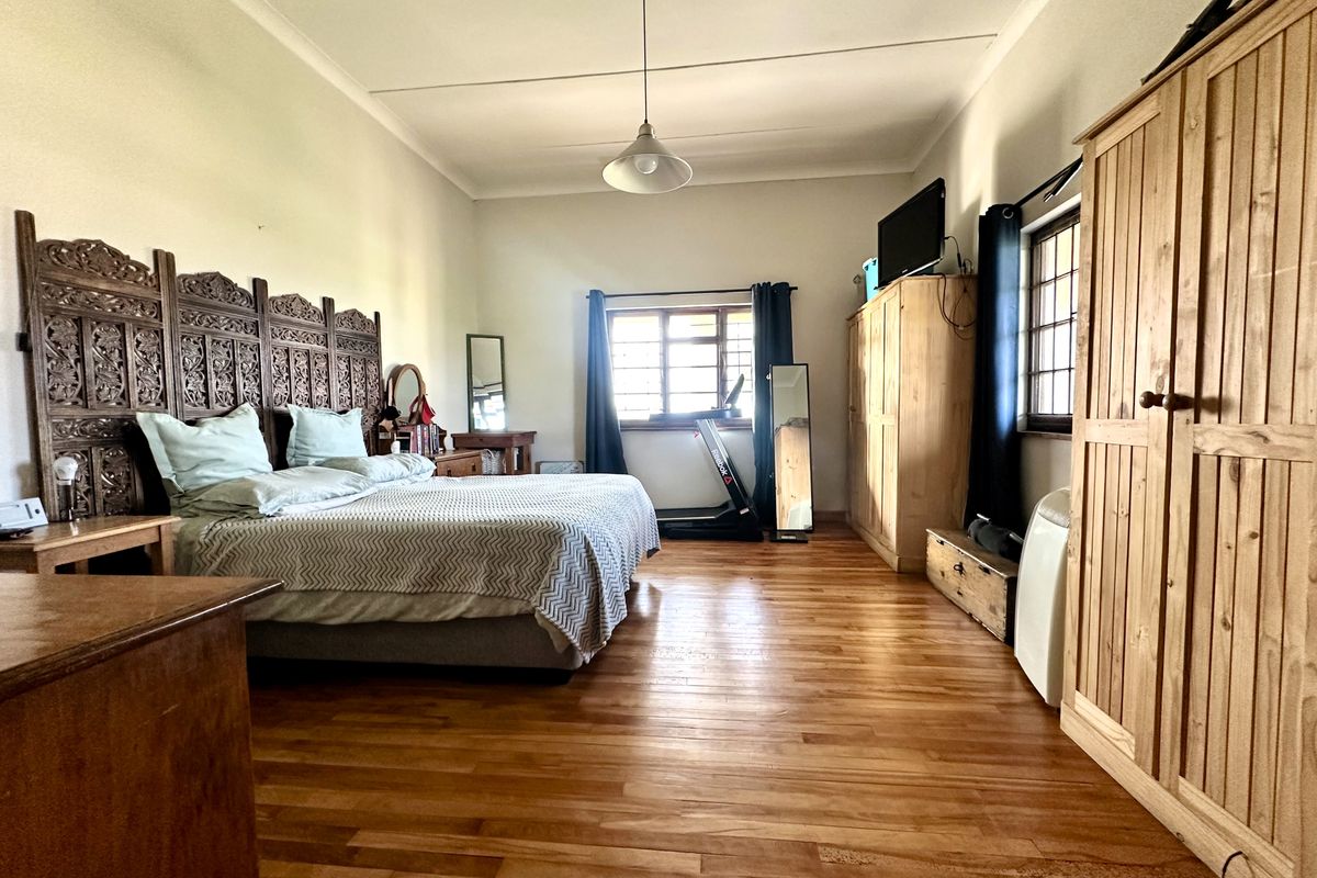 Spacious bedroom featuring warm hardwood flooring, large windows for natural light, and a neutral color palette.