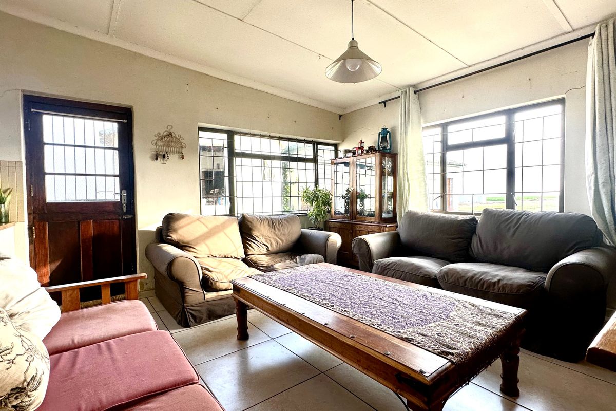 A living room featuring tiled floors, steel-framed windows with security bars, and a timber door, showing signs of wear and requiring cosmetic updates.