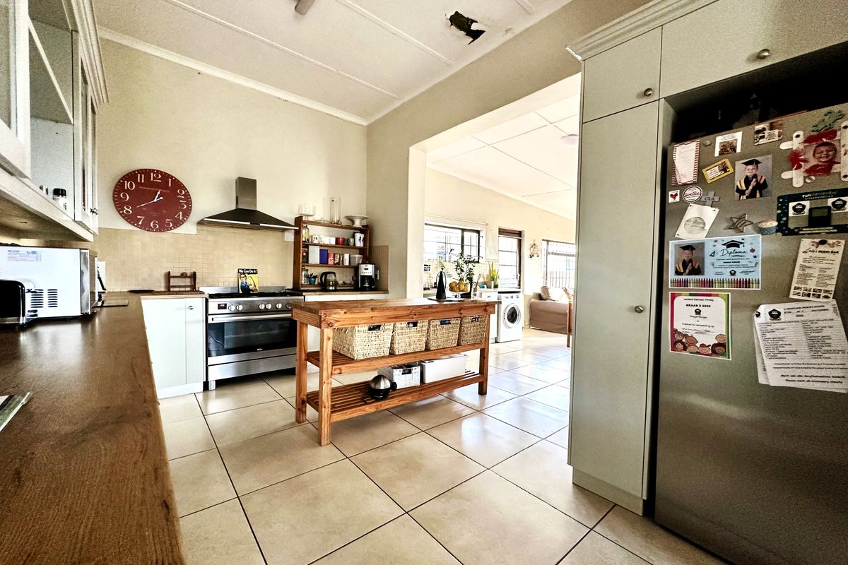 A functional kitchen featuring tiled flooring, built-in cabinetry, and a stainless steel oven with extractor fan, opening into an adjacent living area.