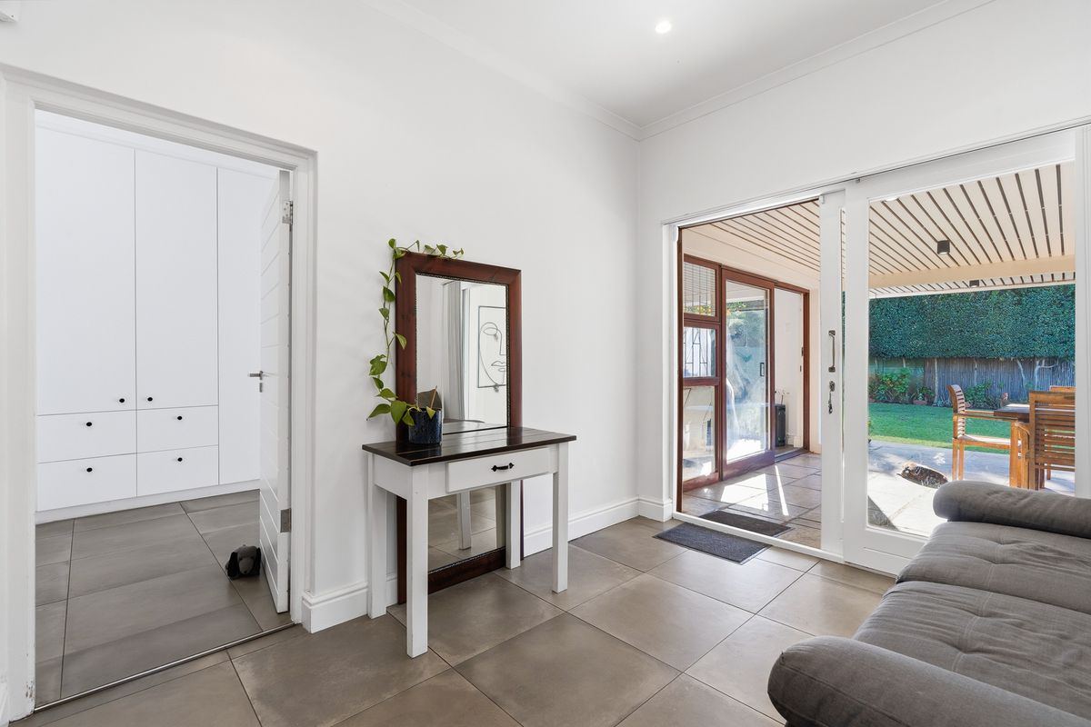 Bright living area featuring large sliding glass doors that open onto a covered patio and garden, with tiled flooring and built-in cabinetry.