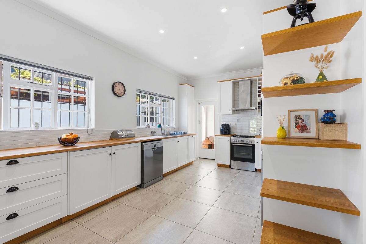 Modern kitchen featuring white cabinetry, timber countertops, tiled flooring, stainless steel oven, extractor fan, and integrated dishwasher.
