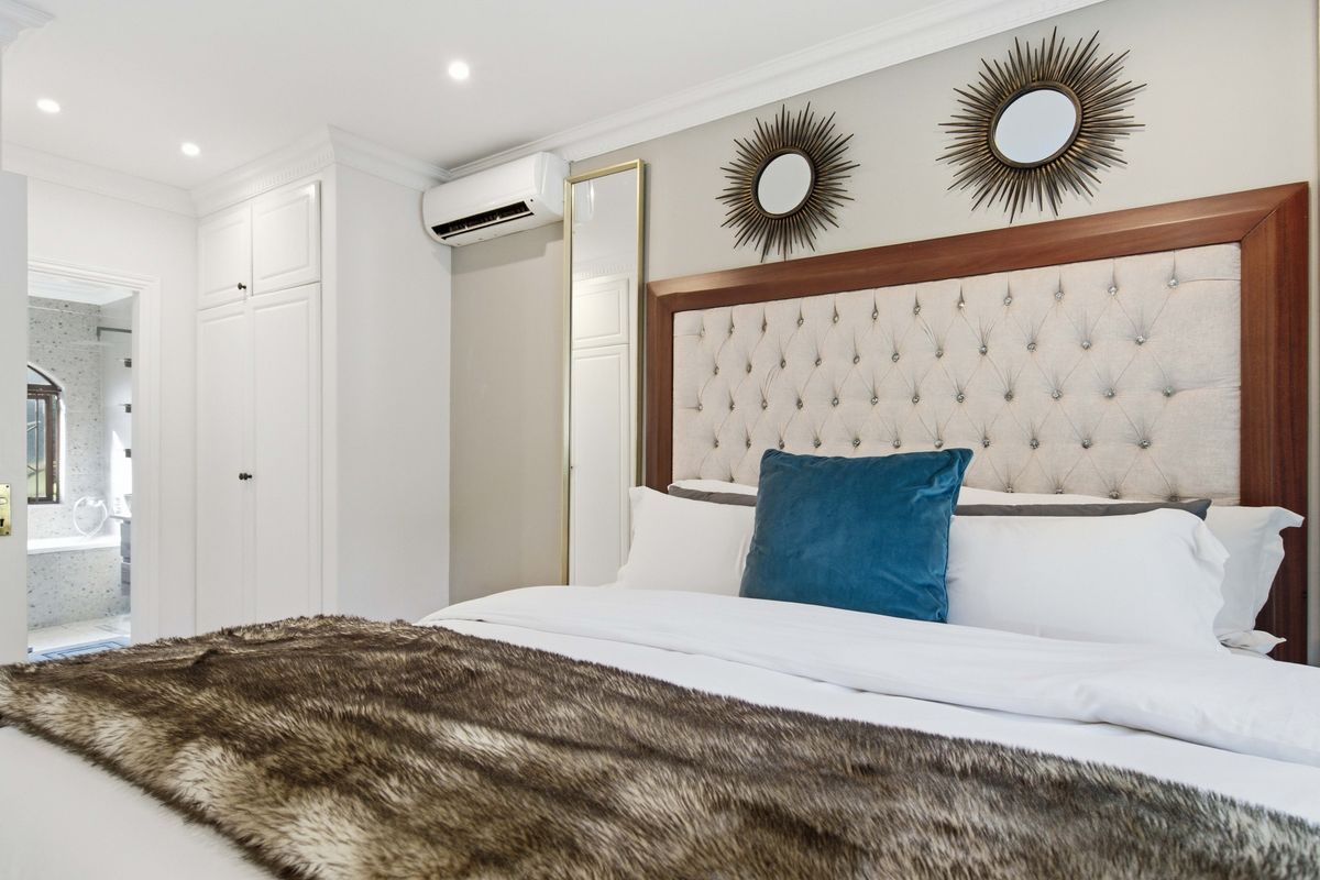 Well-appointed bedroom featuring built-in cupboards, recessed lighting, and a split-system air conditioner, with direct access to an en-suite bathroom.