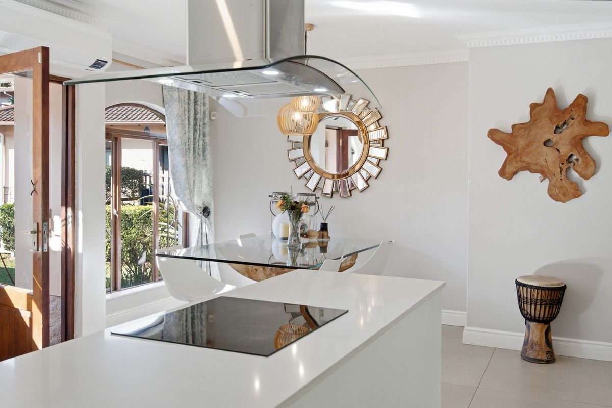 Modern kitchen featuring a central island with an integrated induction hob, overhead extractor fan, and sleek tiled flooring, opening to an outdoor area.