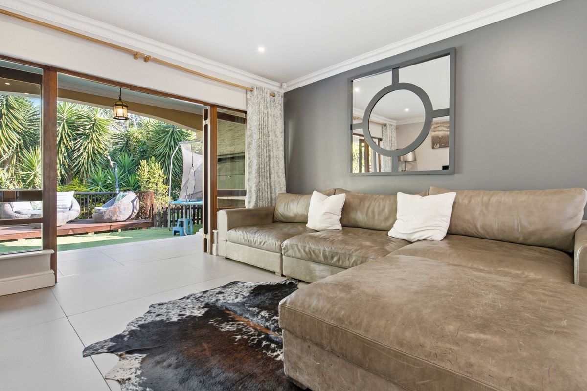 Bright living room featuring large sliding glass doors that open onto a covered patio, with neutral tiled flooring and modern crown molding.