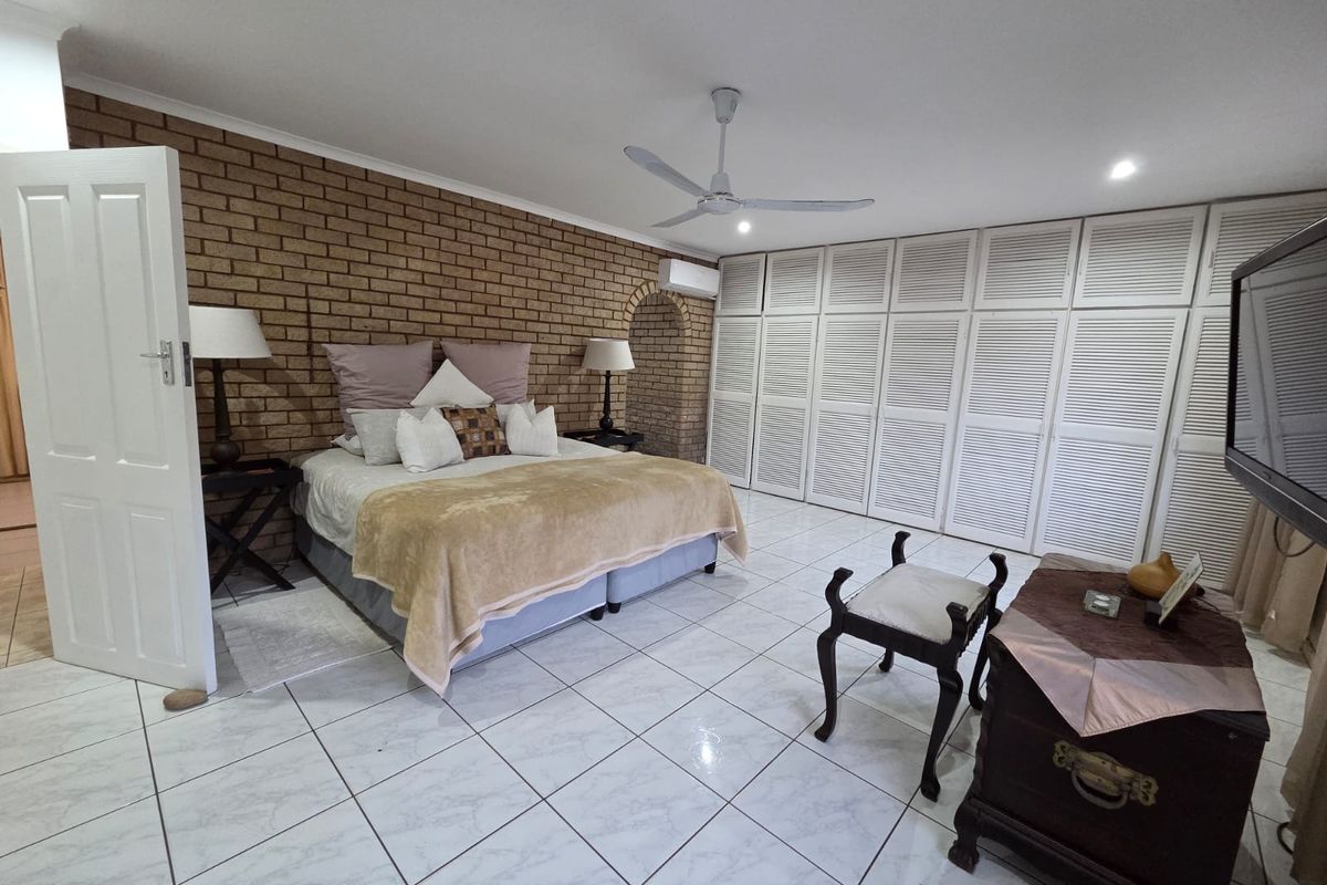 Spacious bedroom featuring an exposed brick feature wall, extensive built-in cupboard storage, tiled flooring, and a ceiling fan for climate control.