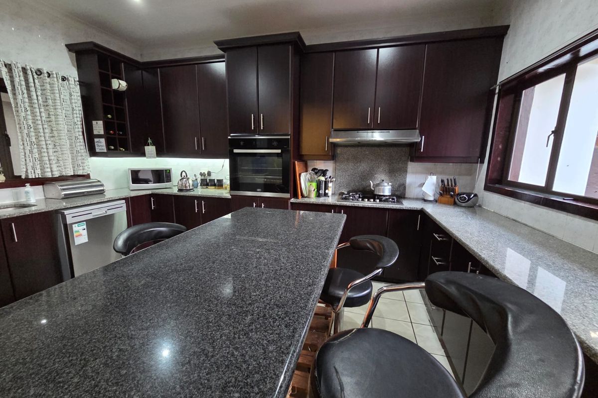 A functional kitchen featuring dark wood cabinetry, granite countertops, a central island, and built-in appliances including an oven and gas hob.