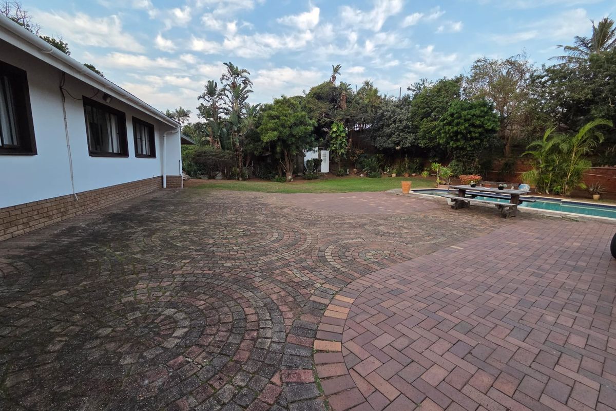 Spacious rear exterior featuring a large paved patio area, swimming pool, and established garden surroundings.