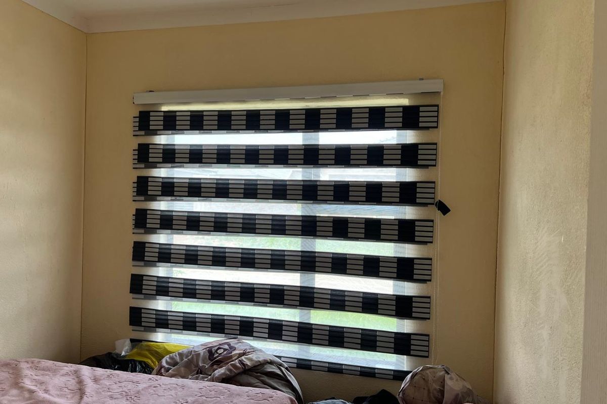 A bedroom featuring a window with modern striped roller blinds and neutral wall finishes.