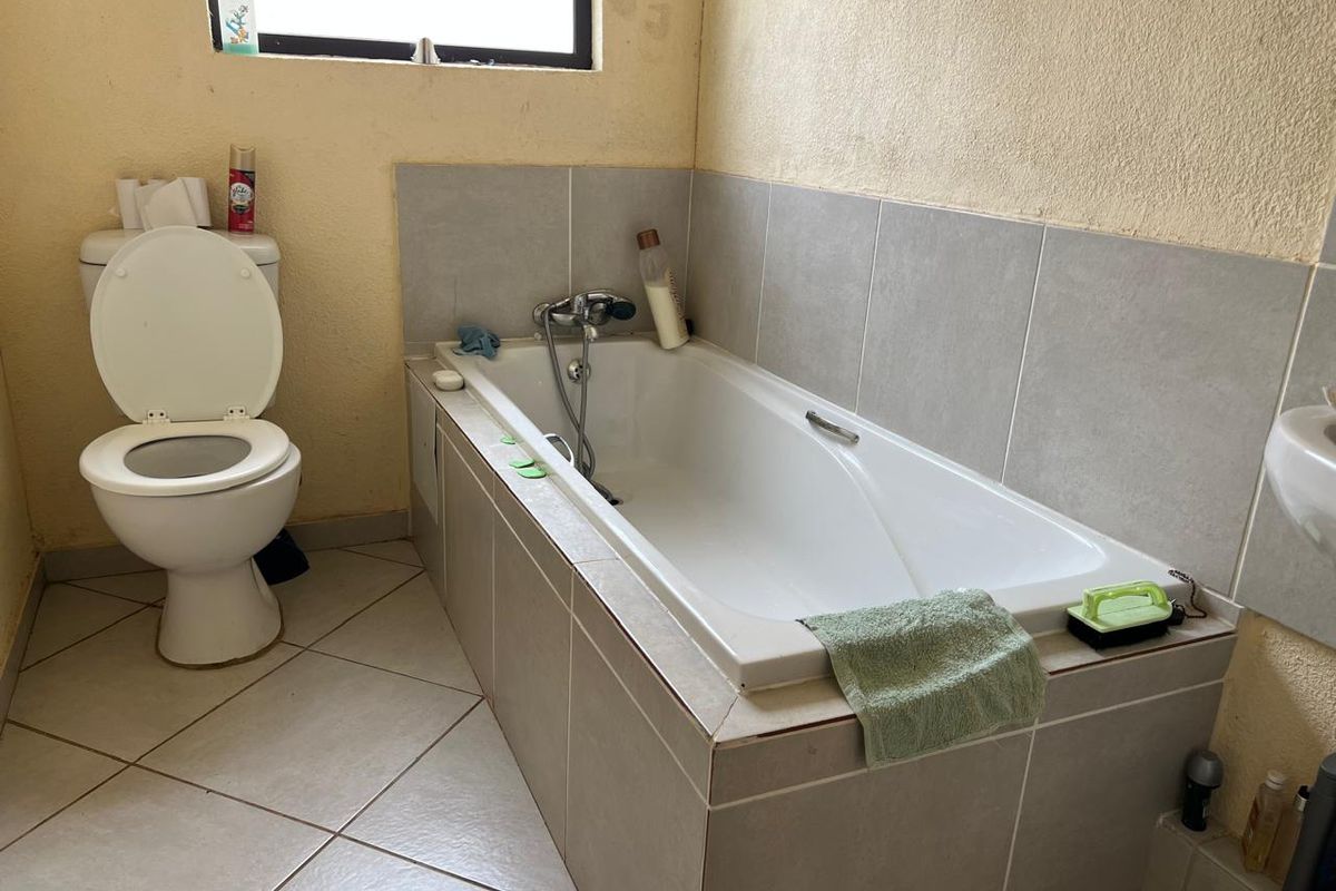 A functional bathroom featuring a built-in bathtub with shower mixer and a standard toilet, finished with neutral wall and floor tiles.