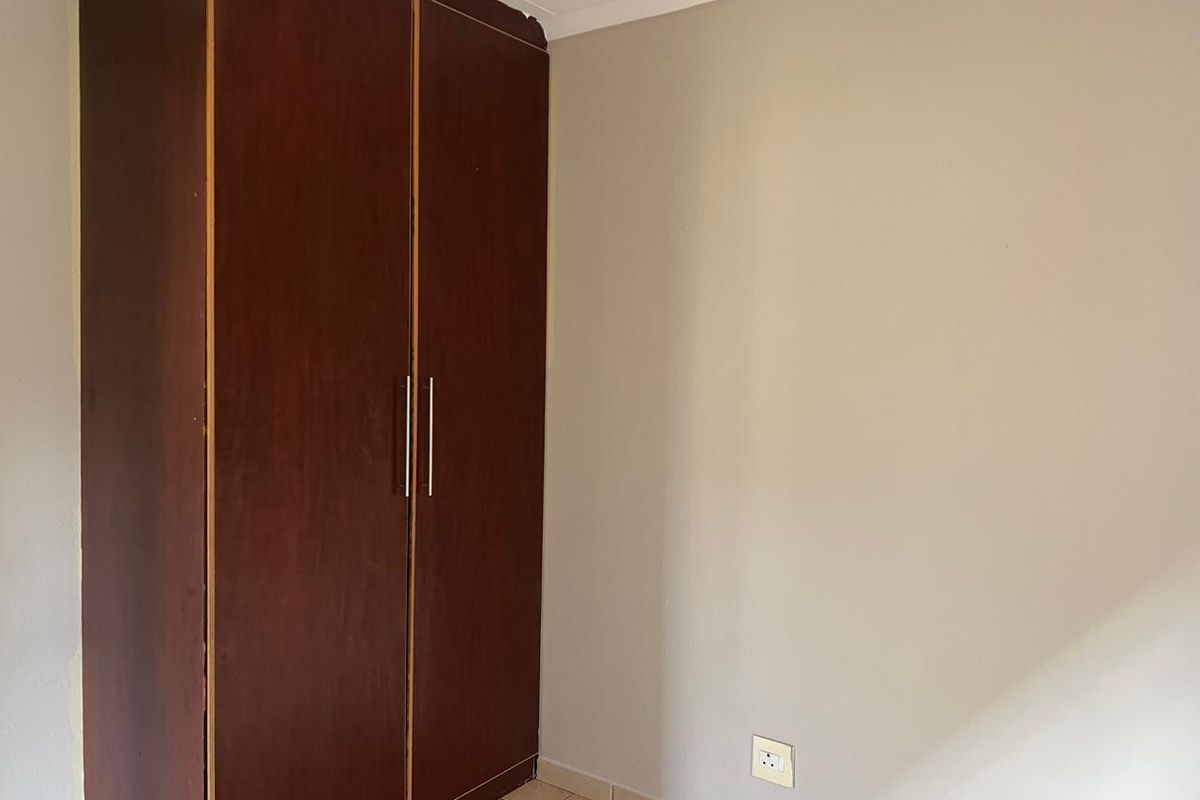 A bedroom interior featuring a built-in dark wood wardrobe and neutral wall finishes with tiled flooring.