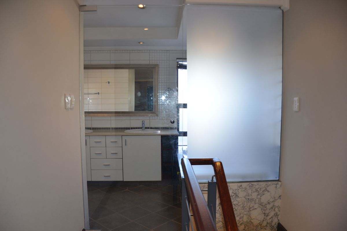 A clean, modern bathroom featuring a vanity with basin, tiled flooring, and a frosted glass partition, viewed from an adjacent hallway.