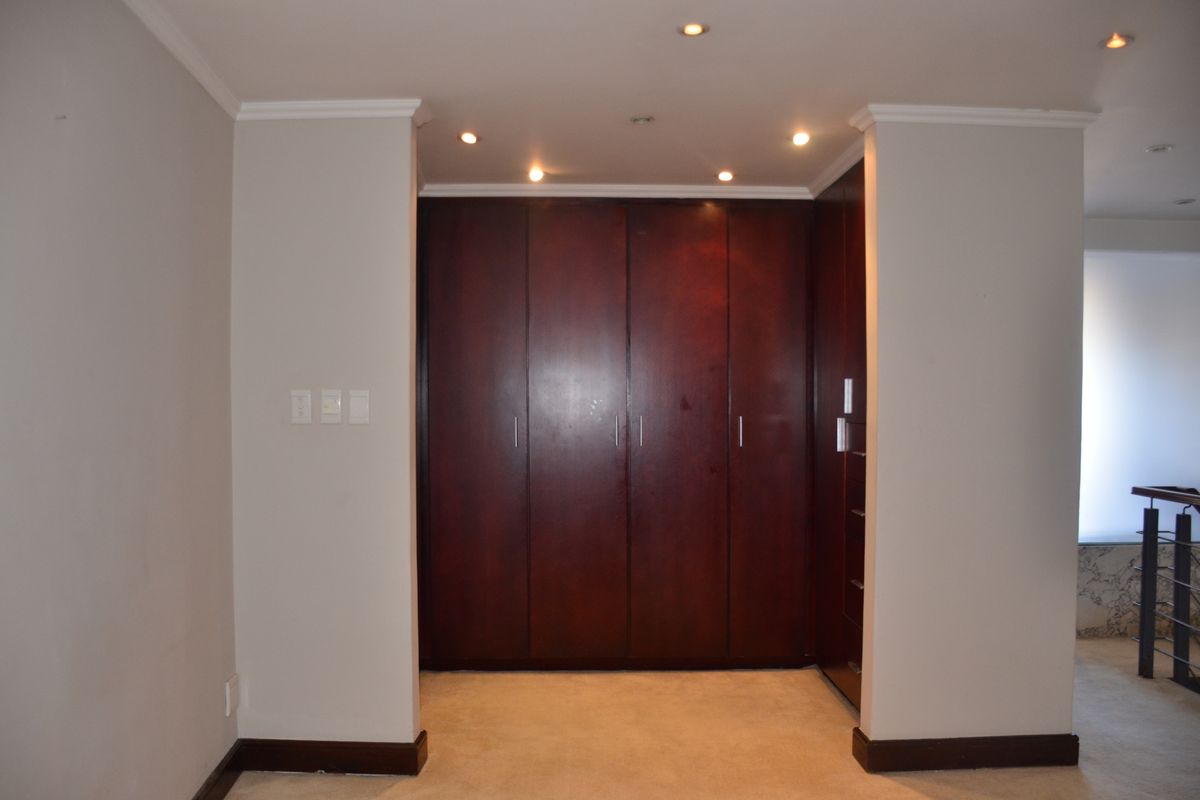 A bedroom interior featuring dark wood built-in cupboards, recessed ceiling lighting, and neutral wall finishes.