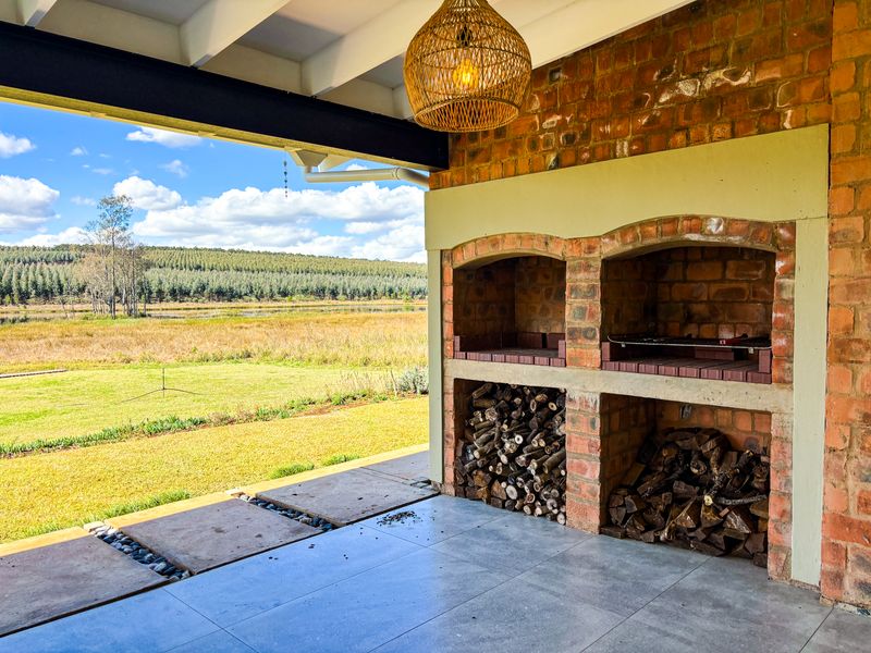 Covered patio featuring a built-in brick braai and tiled flooring, overlooking a scenic landscape with expansive green fields.