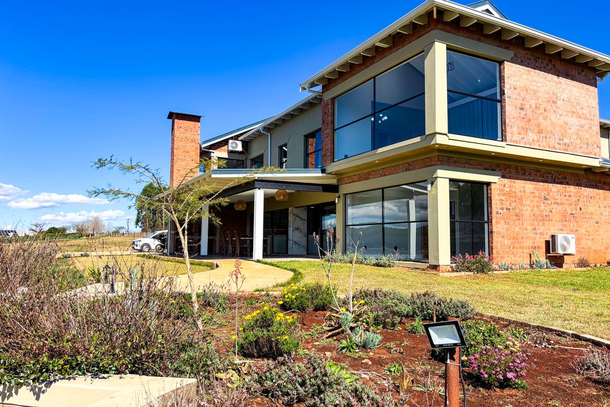 A modern double-story brick home featuring large glass windows, a covered patio area, and a well-maintained landscaped garden.