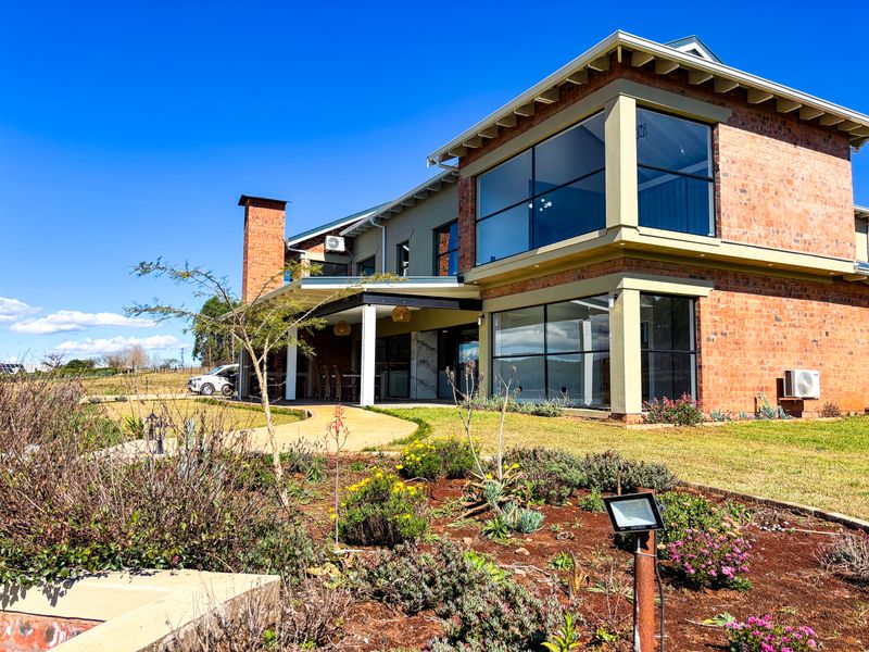 A modern double-story brick home featuring large glass windows, a covered patio area, and a well-maintained landscaped garden.