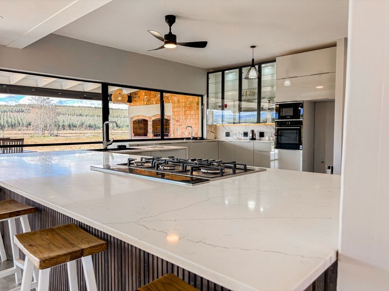 Modern kitchen featuring a large island with a gas hob, stone countertops, integrated appliances, and expansive windows offering scenic views.