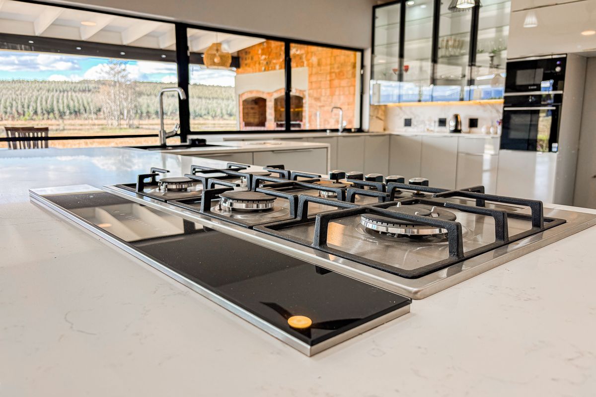 Modern kitchen featuring a large island with a built-in gas cooktop, quartz countertops, and sleek cabinetry, overlooking a scenic outdoor area.