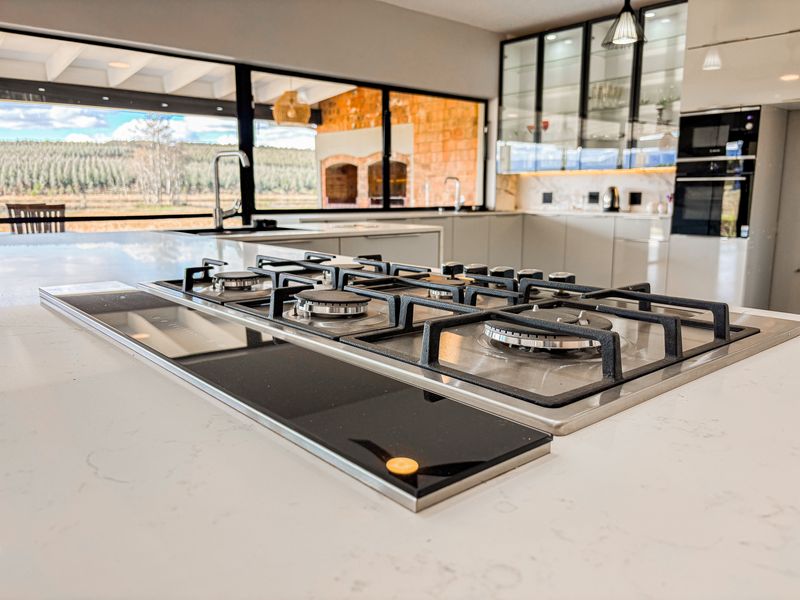 Modern kitchen featuring a large island with a built-in gas cooktop, quartz countertops, and sleek cabinetry, overlooking a scenic outdoor area.