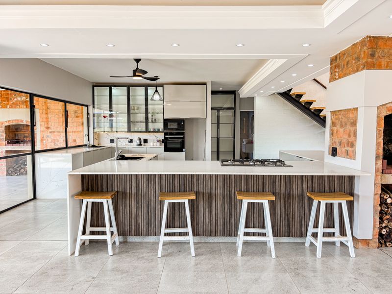 Modern open-plan kitchen featuring a large island with stone countertops, built-in appliances, exposed brick accents, and a sleek staircase, creating a sophisticated living space.