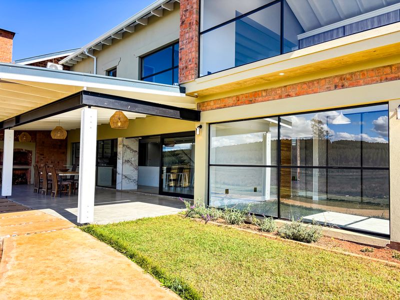 A modern rear exterior view featuring a spacious covered patio, large glass sliding doors, and exposed brick accents overlooking a landscaped garden.