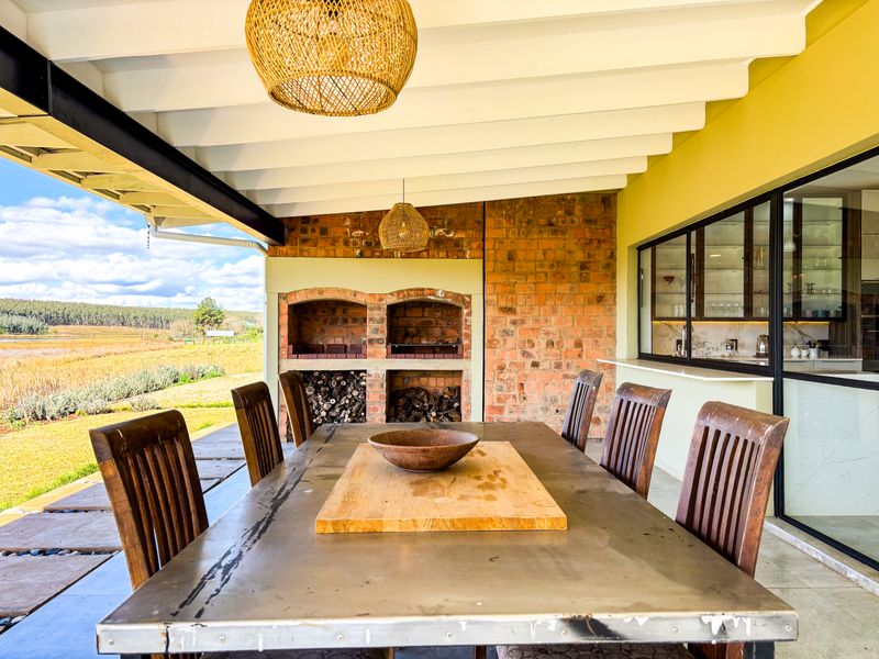 Covered outdoor patio featuring a built-in brick braai, exposed beam ceiling, and direct access to the garden with scenic rural views.