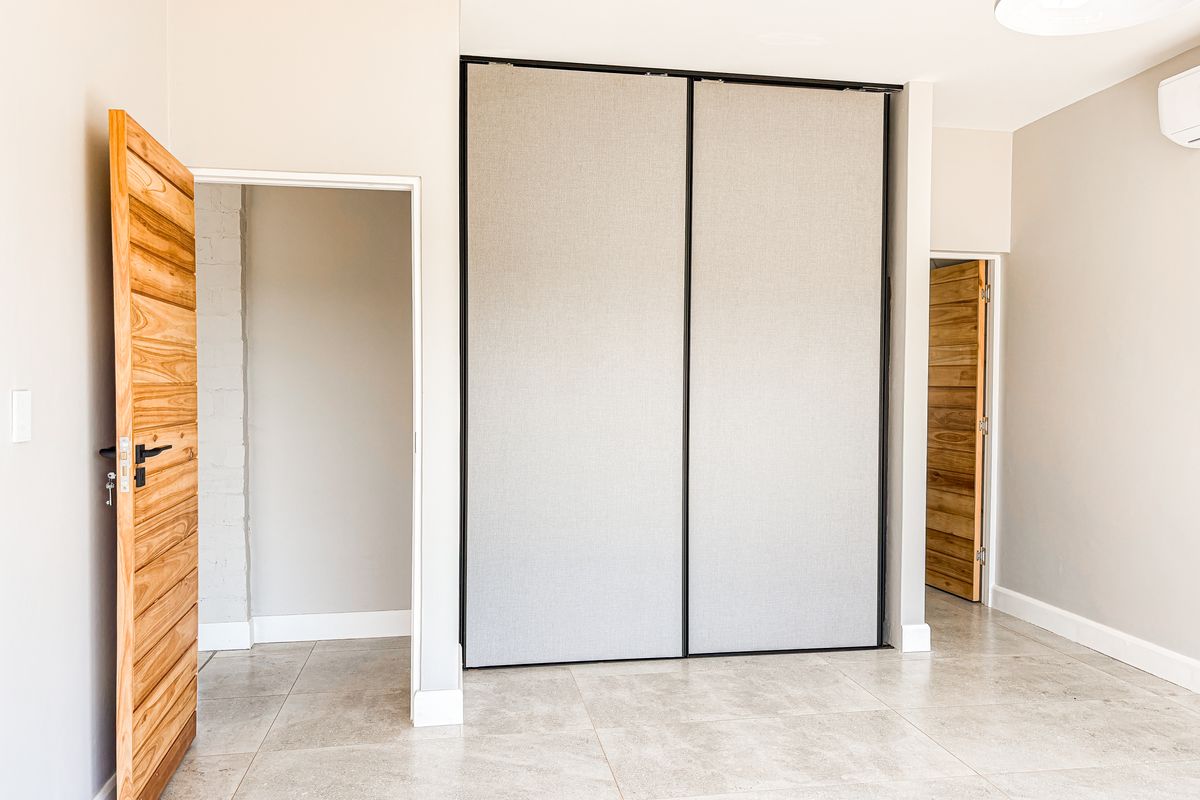 A bright, modern bedroom featuring neutral tiled flooring, built-in sliding wardrobes, and timber doors, providing a clean and versatile living space.