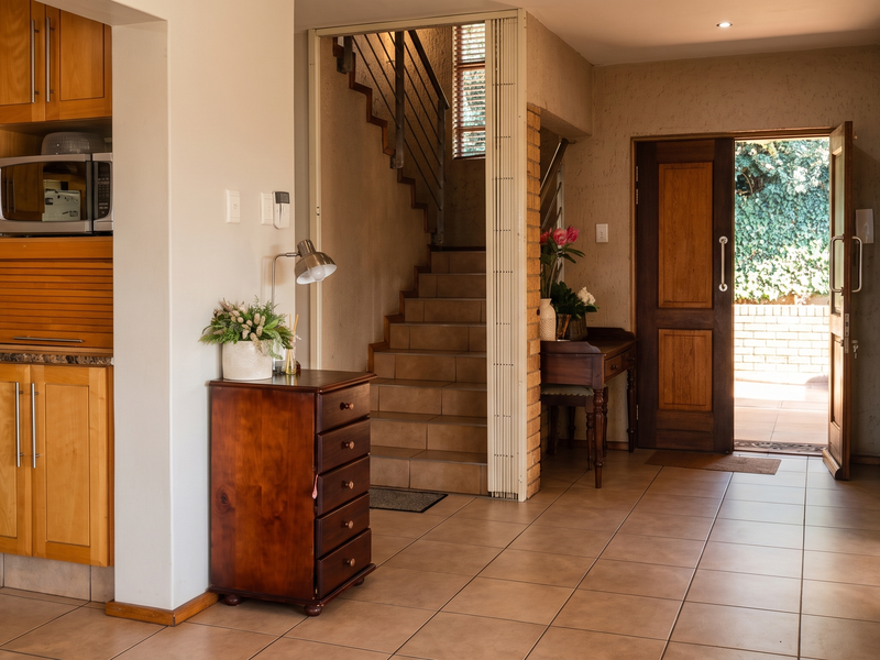 Open plan kitchen area featuring wooden cabinetry and tiled flooring, leading to a staircase and the main entrance door.