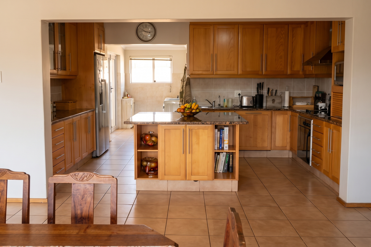 Spacious kitchen featuring wooden cabinetry, granite countertops, a central island, and integrated appliances, flowing into an adjacent utility area.