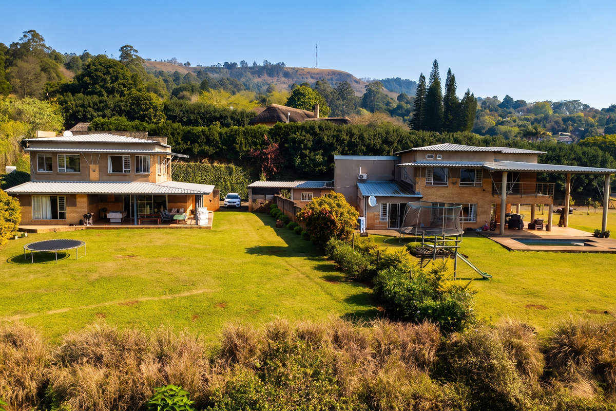 Aerial view of a large residential property featuring two main structures, expansive lawns, a swimming pool, and a covered patio area.