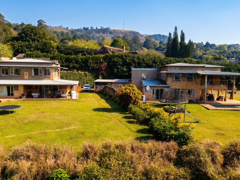 Aerial view of a large residential property featuring two main structures, expansive lawns, a swimming pool, and a covered patio area.