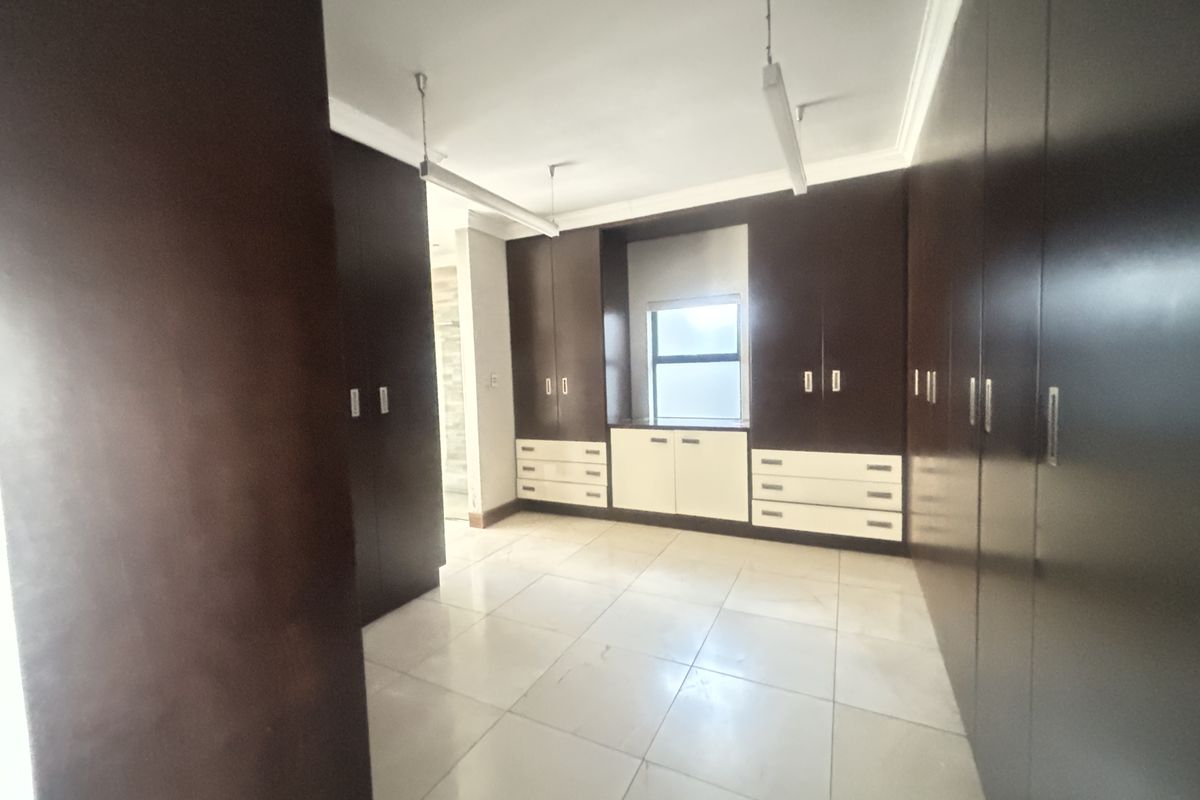 Spacious bedroom featuring extensive dark wood built-in cabinetry, light-colored tiled flooring, and ample natural light from a central window.