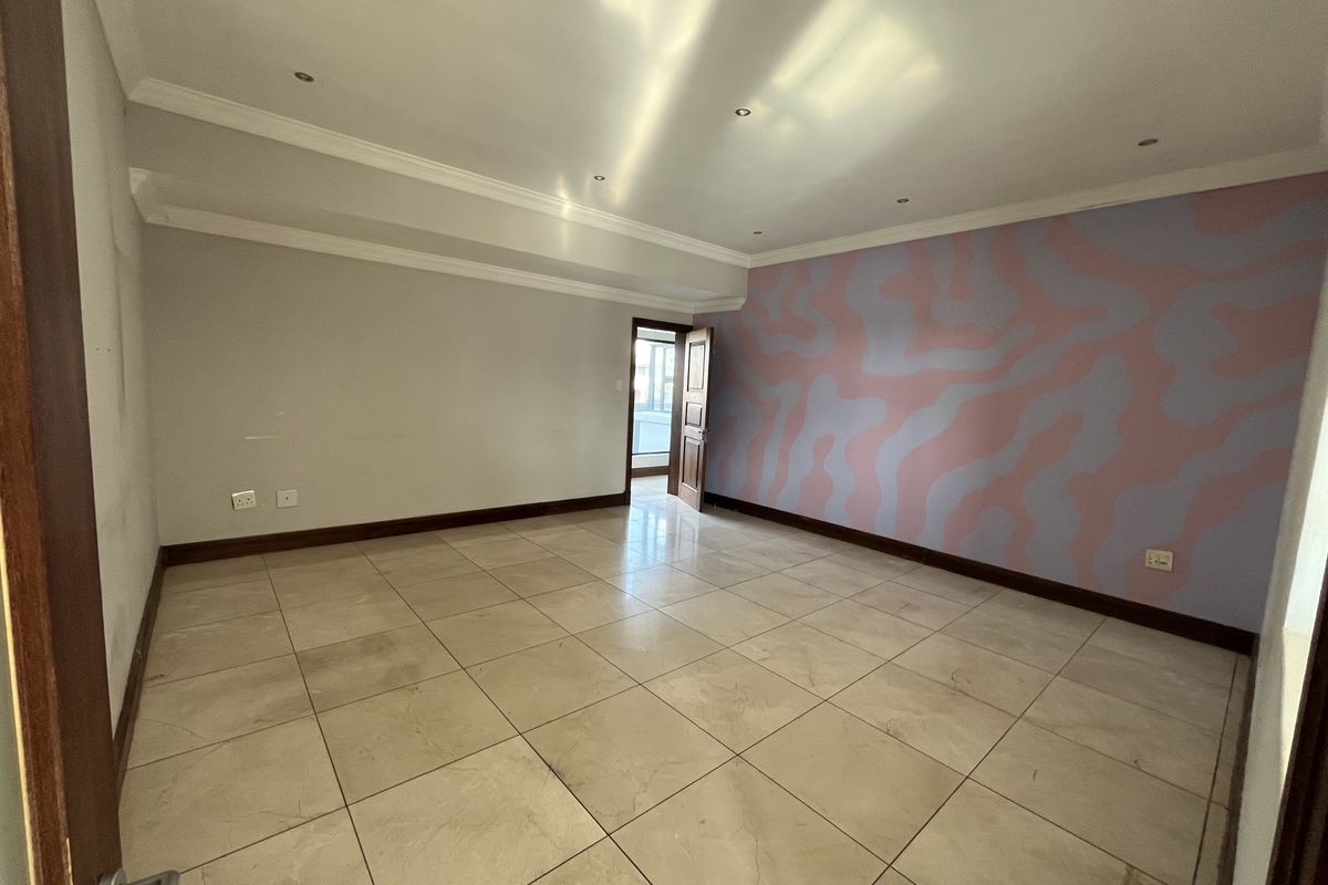 An empty living room featuring tiled flooring, recessed downlighting, and a coved ceiling, with a decorative accent wall.