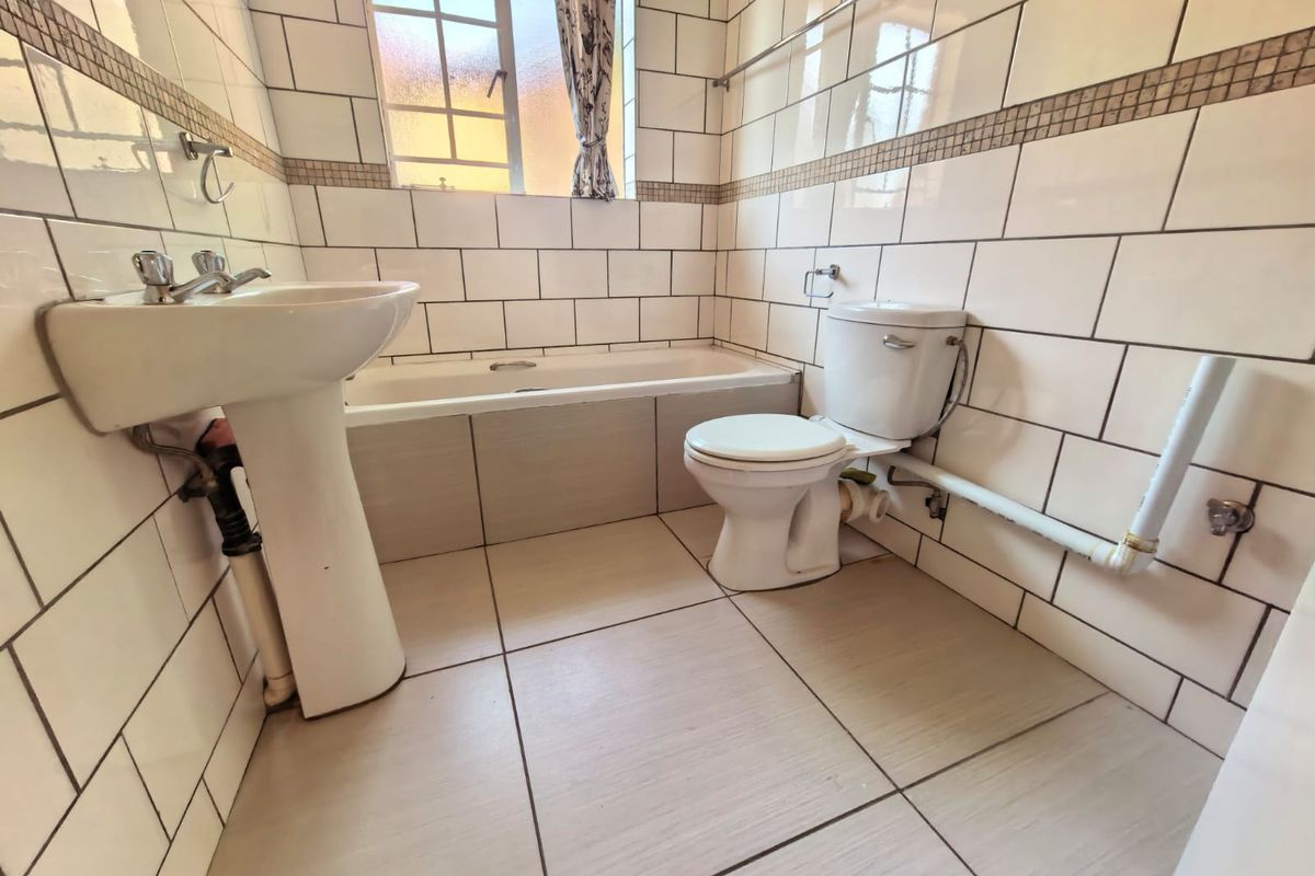 A functional bathroom featuring a pedestal basin, standard toilet, and a built-in bathtub with tiled walls and flooring.