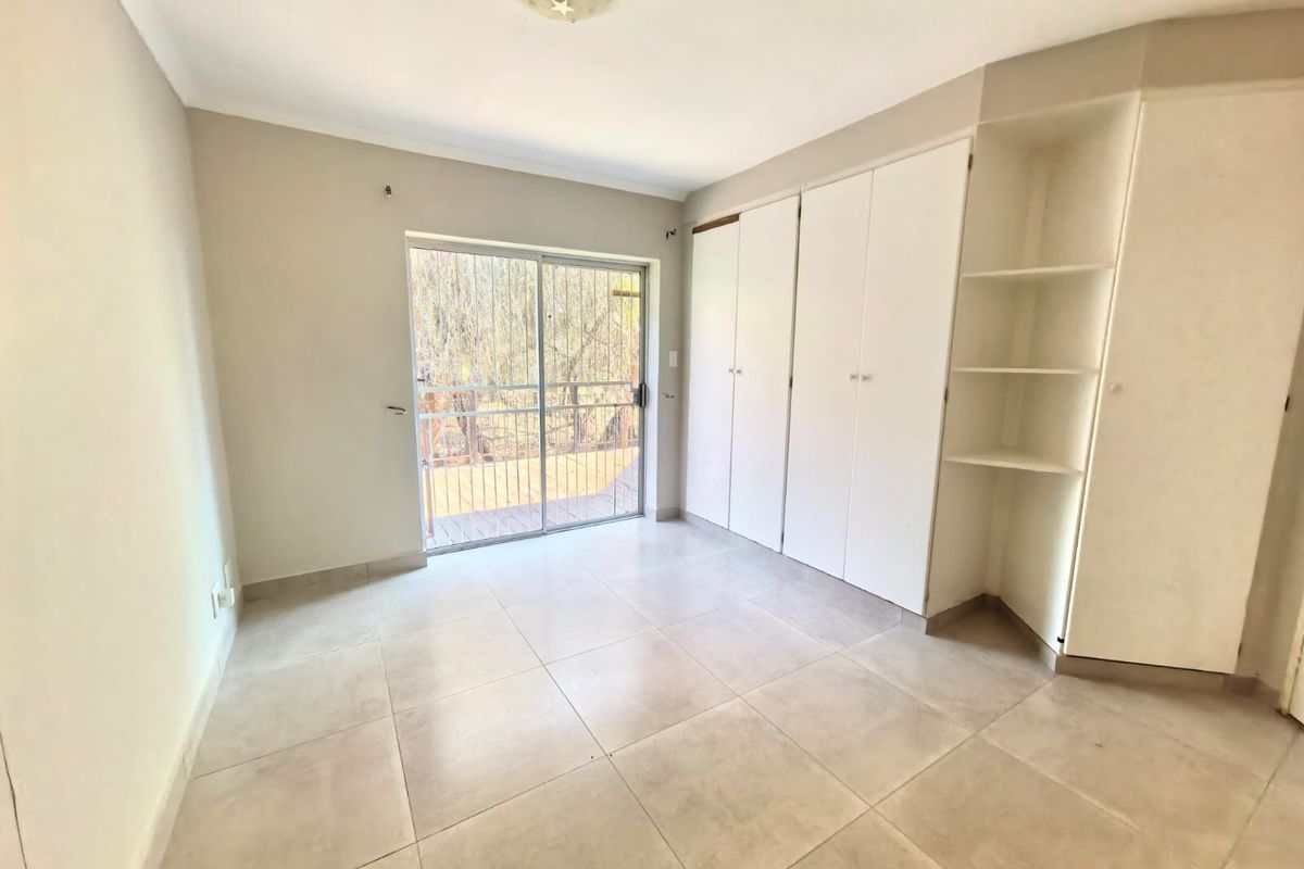 A bright, empty bedroom featuring built-in cabinetry with shelving and sliding glass doors leading to an outdoor area.