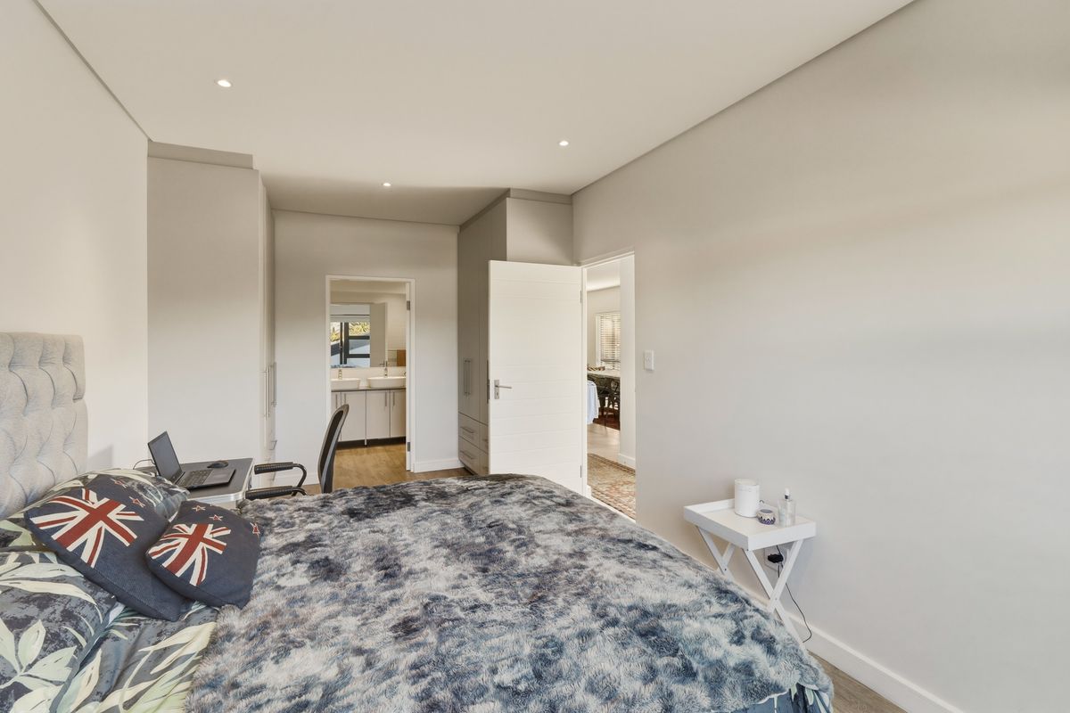 A well-maintained bedroom featuring neutral finishes, recessed downlighting, and convenient access to an en-suite bathroom with built-in storage.