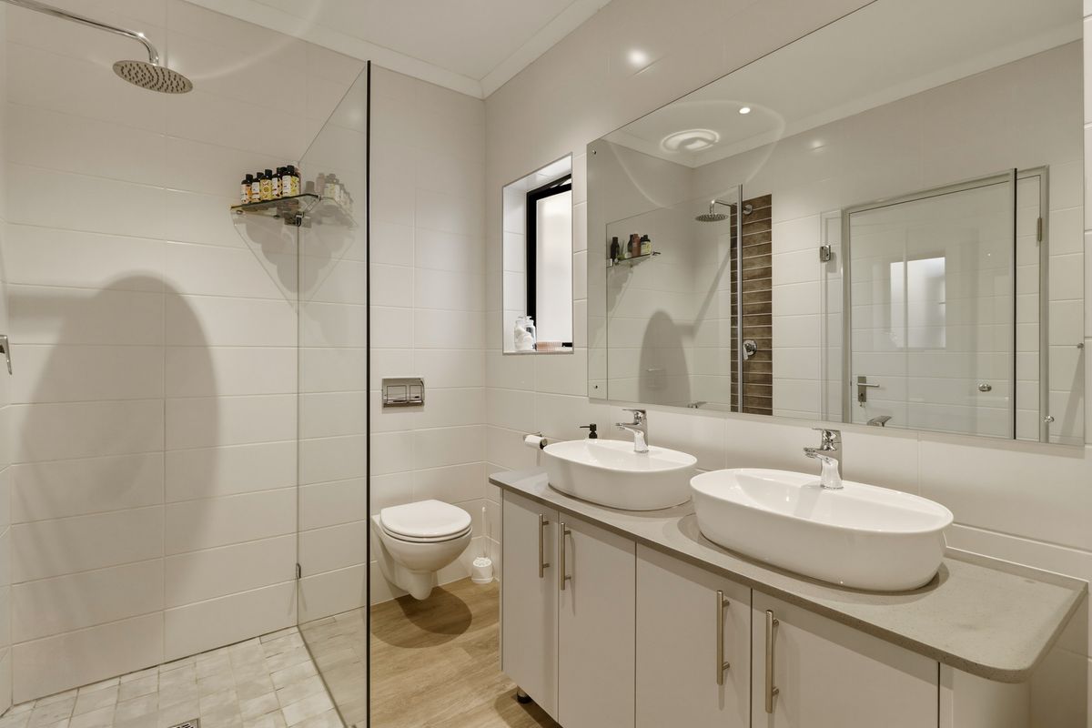 Modern bathroom featuring a double vanity with vessel sinks, a wall-hung toilet, and a spacious walk-in shower with a rain shower head.