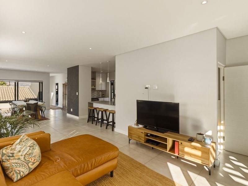 Spacious open-plan living area featuring tiled floors, recessed lighting, and a modern kitchen with a breakfast bar, seamlessly flowing to the dining space.
