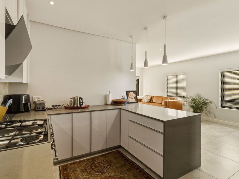 Modern open-plan kitchen featuring sleek cabinetry, stone countertops, gas hob, and integrated extractor, flowing seamlessly into a bright living area with tiled floors.