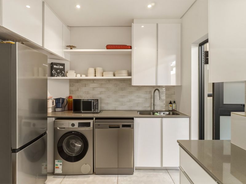 Modern, well-appointed scullery featuring sleek white cabinetry, stone countertops, subway tile backsplash, and integrated space for laundry and dishwashing appliances.