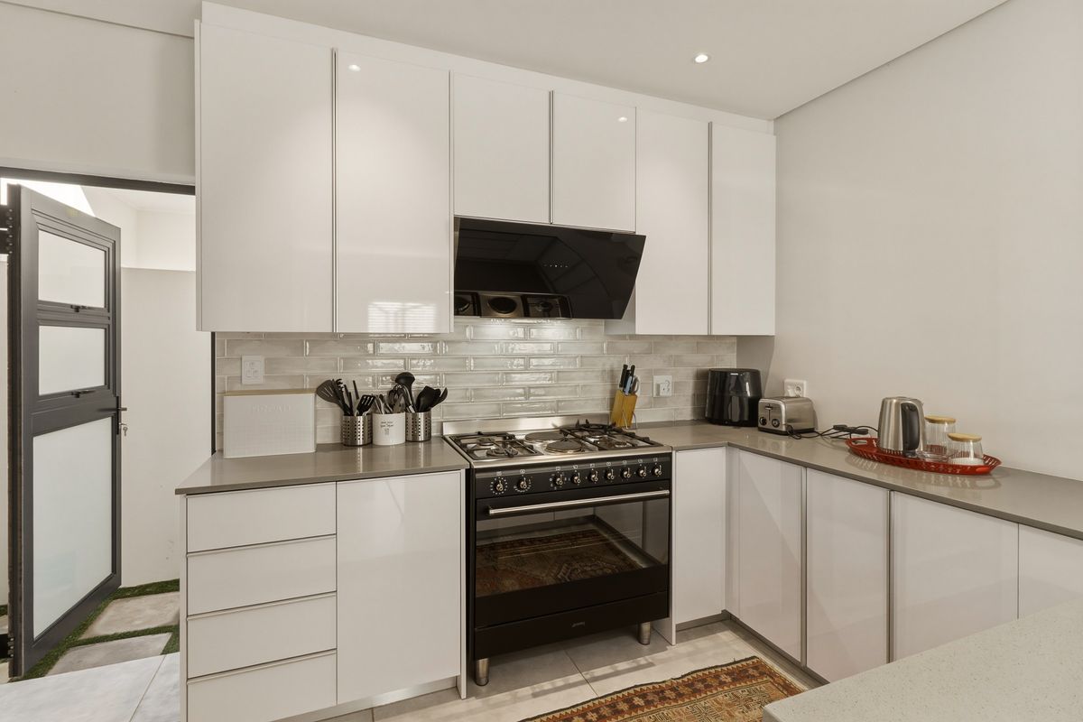 Modern kitchen featuring sleek white cabinetry, stone countertops, a subway tile backsplash, and a high-quality gas stove with an integrated extractor fan.