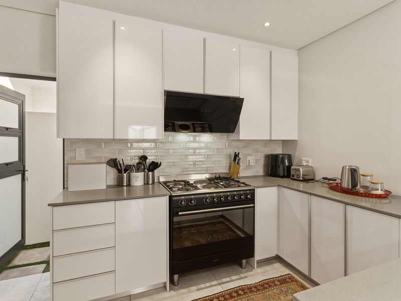 Modern kitchen featuring sleek white cabinetry, stone countertops, a subway tile backsplash, and a high-quality gas stove with an integrated extractor fan.