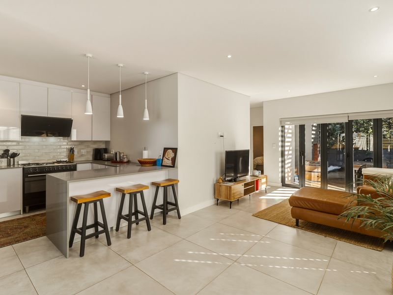 Modern open-plan living area featuring a sleek kitchen with stone countertops, gas stove, and seamless flow to the outdoor patio through bi-fold doors.