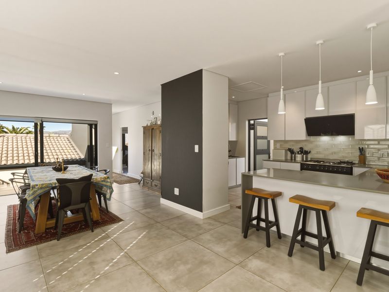 Modern open-plan kitchen and dining area featuring sleek cabinetry, stone countertops, gas hob, and large sliding doors leading to an outdoor space.