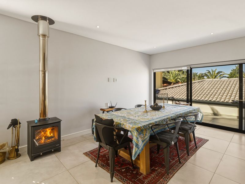 A bright dining area featuring a modern freestanding fireplace with a stainless steel flue, tiled flooring, and large sliding doors leading to an outdoor space.