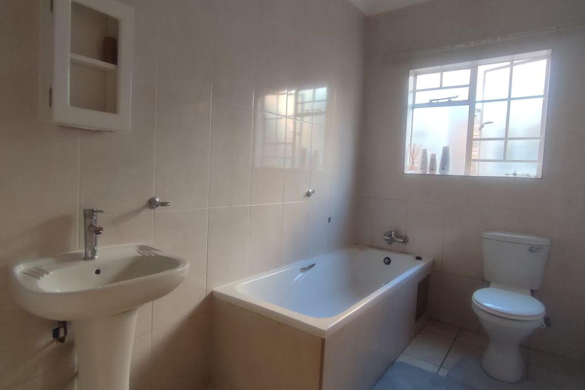 A functional bathroom featuring a pedestal washbasin, bathtub, and toilet with neutral wall tiling and natural light from a window.