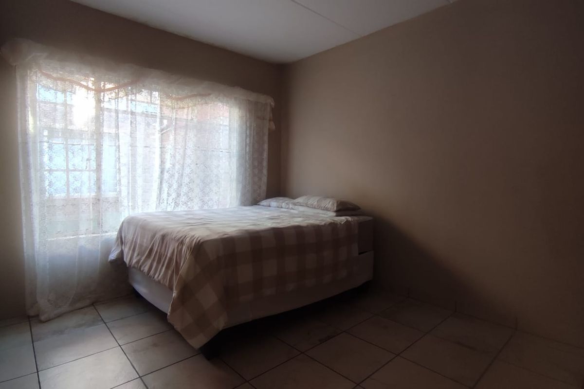 A simple bedroom featuring tiled flooring and a built-in cupboard, offering a functional space with natural light from the window.