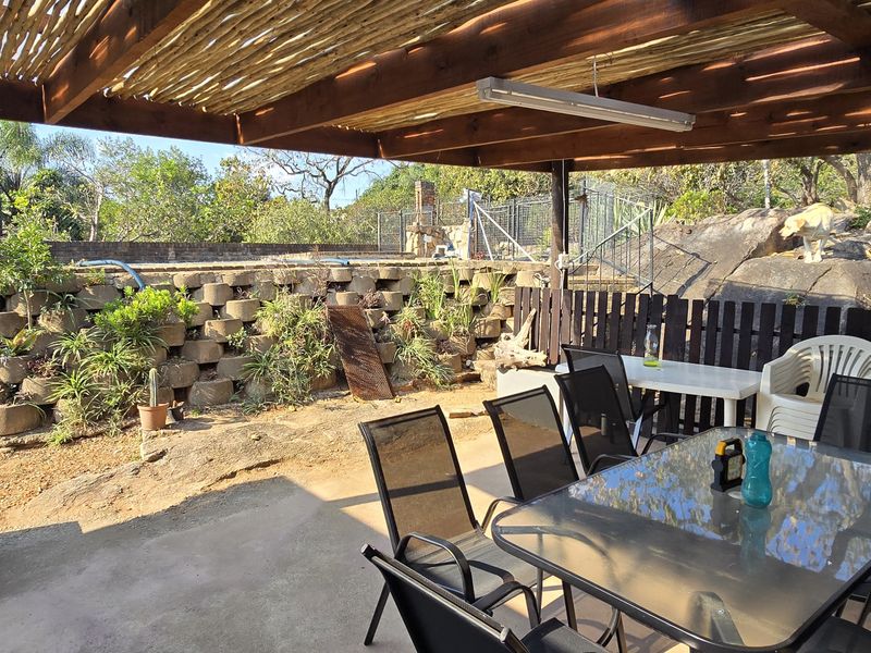 Covered outdoor patio area featuring a timber pergola structure, overlooking a tiered garden with natural rock formations and a retaining wall.