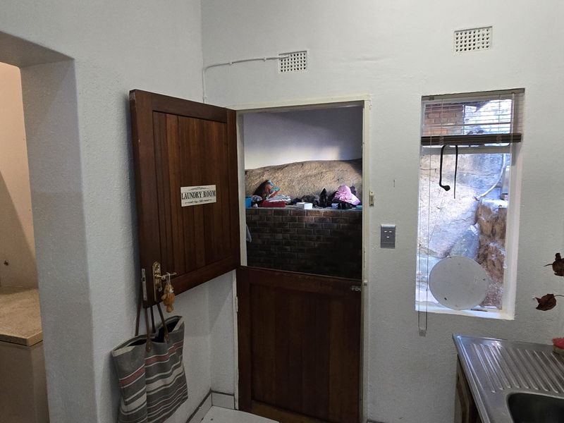 A functional laundry area featuring a stable-style wooden door, stainless steel sink, and direct access to an outdoor rock-faced utility space.