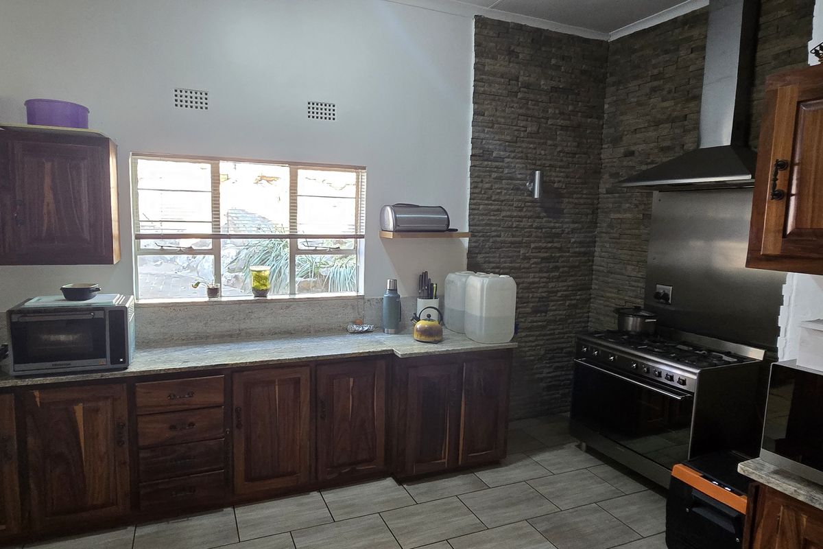 A functional kitchen featuring dark wood cabinetry, granite countertops, a stainless steel gas stove with extractor fan, and a decorative stone feature wall.
